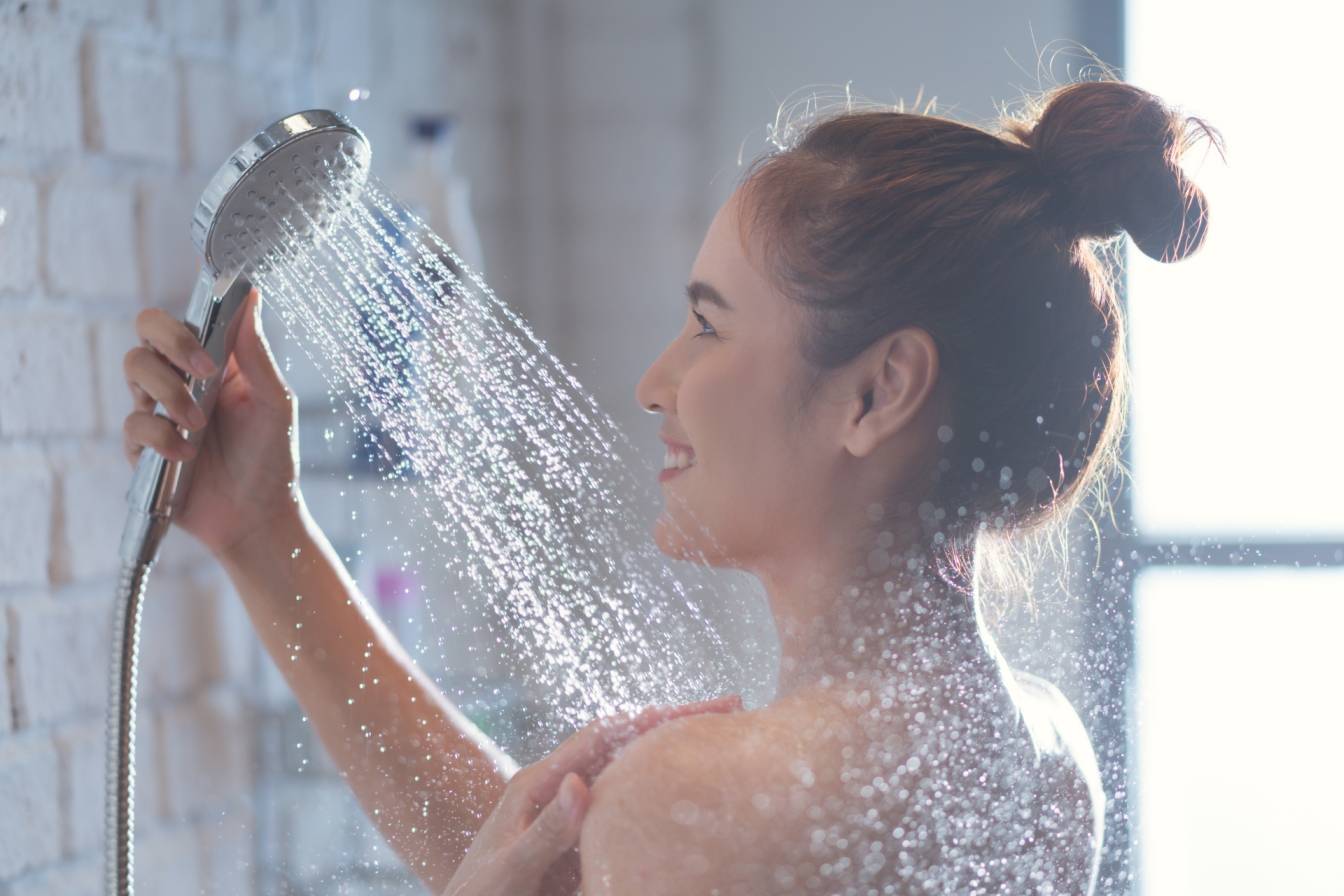 Jak zimny prysznic pomaga ujędrnić skórę? Kobieta polewa się zimnym prysznicem w łazience w swoim domu.