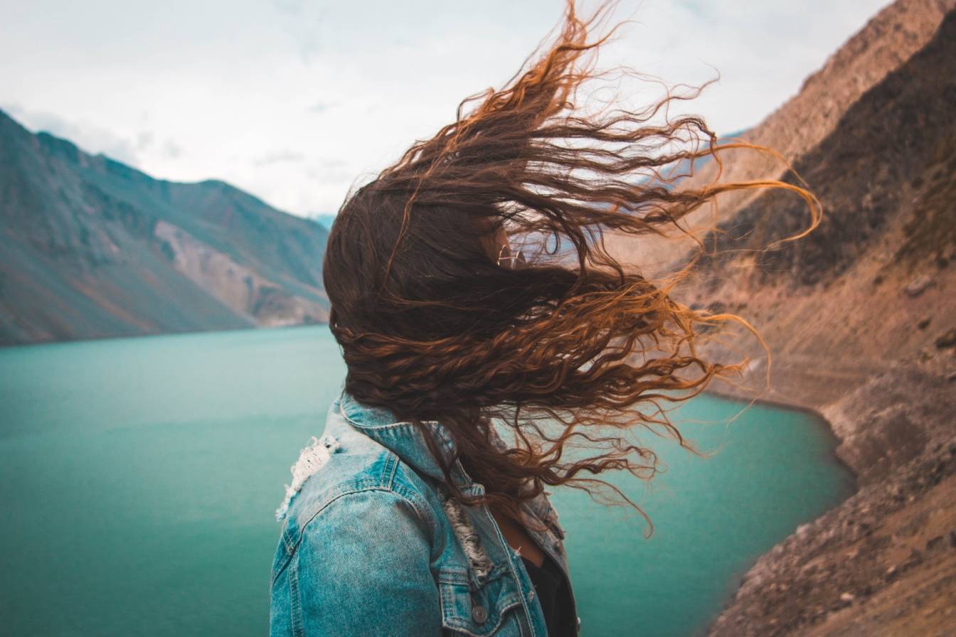 Wiatr to czynnik patogenny w medycynie chińskiej, który atakuje na wiosnę. Kobieta stoi na skarpie nad jeziorem, a jej włosy rozwiewa wiatr.