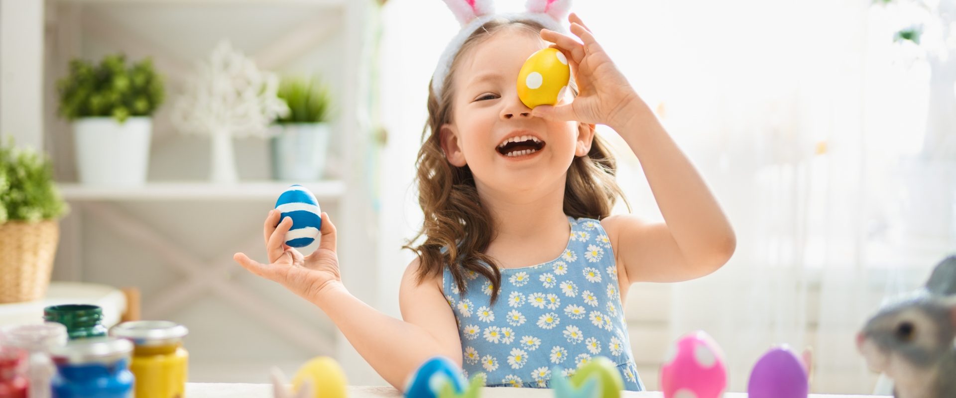 Przepisy na święta wielkanocne autorstwa Agnieszki Żelazko. Dziewczynka w opasce z uszami królika maluje pisanki w kuchni.