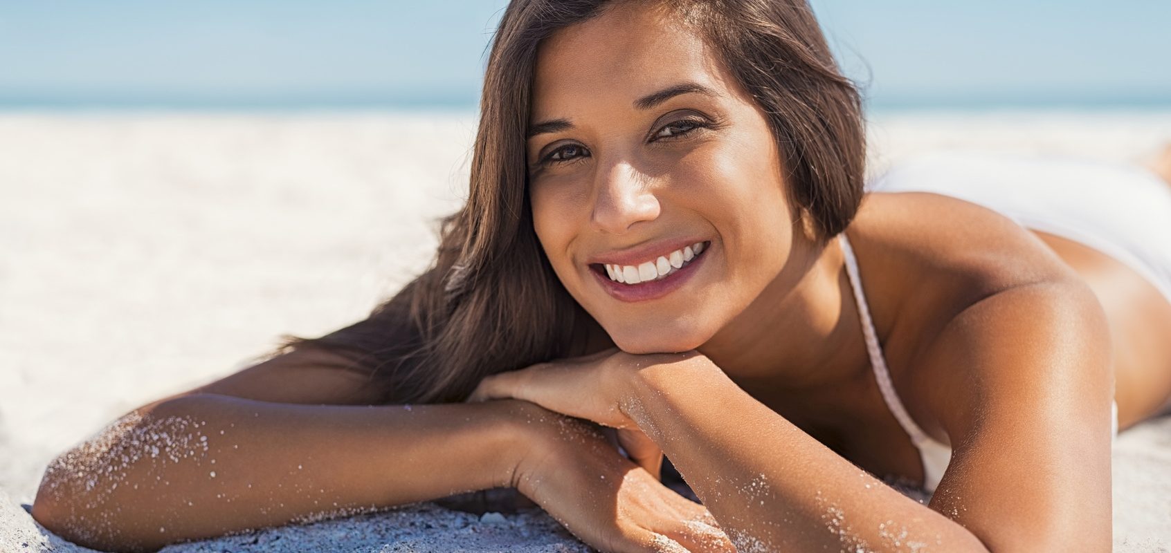 Witamina D3 - w jaki sposób najlepiej ją przyjmować? Uśmiechnięta dziewczyna opala się na plaży nad morzem.