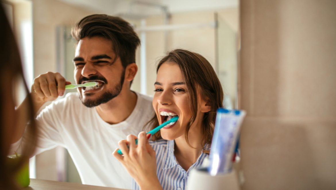 Choroby od zepsutych zębów - jak chory i zepsuty ząb zatruwa organizm? Para myje wspólnie zęby nad umywalką w łazience.