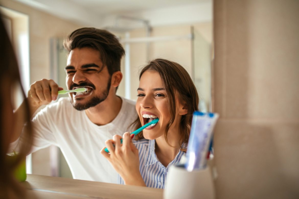 Choroby od zepsutych zębów - jak chory i zepsuty ząb zatruwa organizm? Para myje wspólnie zęby nad umywalką w łazience.
