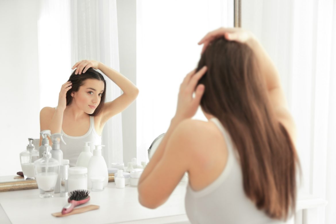 Jak leczyć wypadające włosy? Jakie metody są skuteczne opowiada dr n. med. Olga Warszawik-Hendzel, specjalista dermatolog z kliniki Elite w Warszawie. Młoda kobieta stoi przed lustrem, martwiąc się o wypadające włosy.