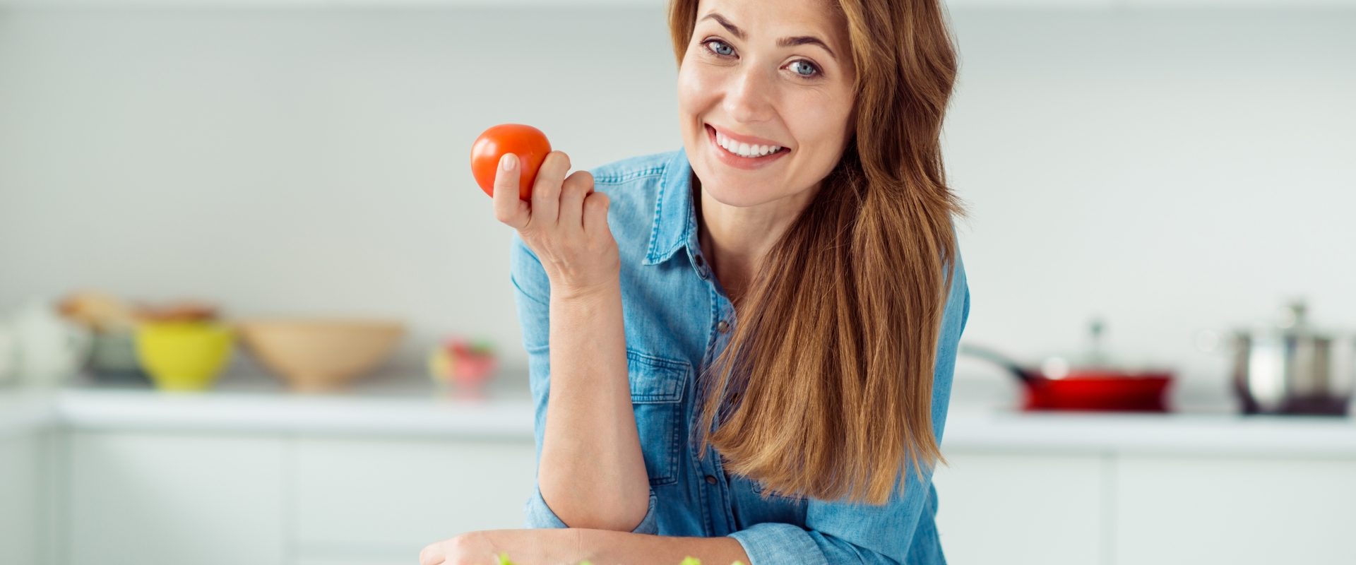 Zakwaszenie organizmu - czym jest i co warto o nim wiedzieć? Kobieta opiera się łokciami o blat kuchenny, trzymając w ręku pomidora.