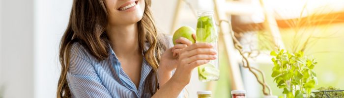 Zakwaszenie żołądka - jakie jest odpowiednie pH kwasu solnego w żołądku? Uśmiechnięta kobieta je jabłko, siedząc przy stole pełnym zdrowej żywności.