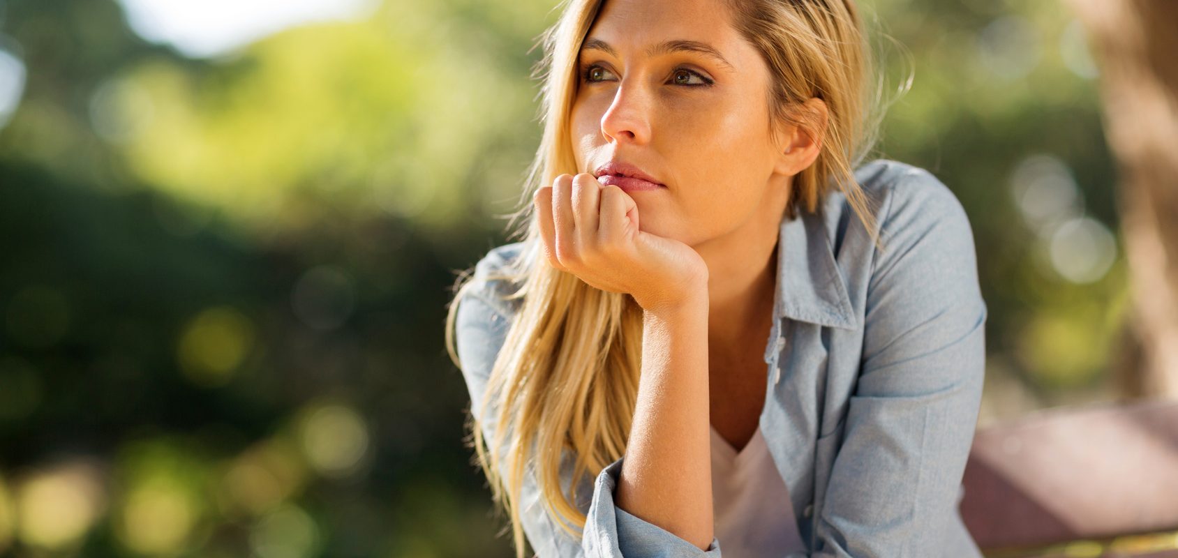 Zespół jelita nadwrażliwego - jak leczyć? Jakie ją objawy zespołu jelita drażliwego? Zamyślona dziewczyna w blond włosach i dżinsowej koszuli opiera się o werandę.