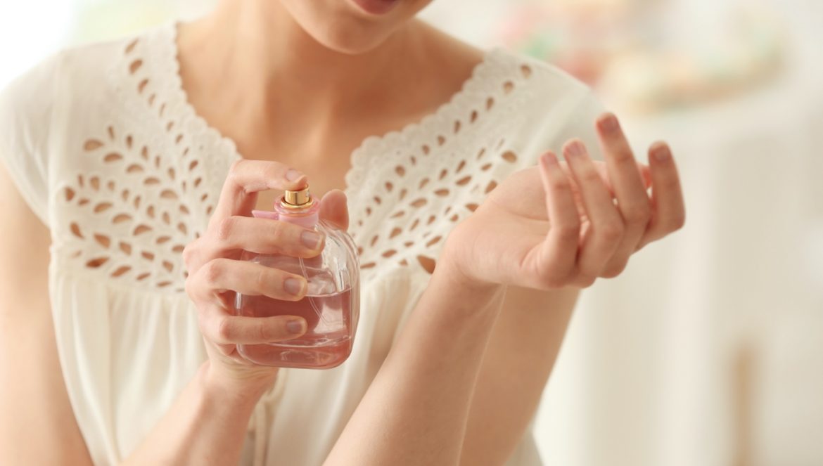 Czy zapach ciała może świadczyć o chorobie? Kobieta w białej boho bluzce pryska nadgarstek perfumami.