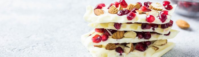 Przepisy na zdrowy deser dla dziecka. Kawałki białej czekolady z nasionami i owocem granatu w formie piramidy z batoników.