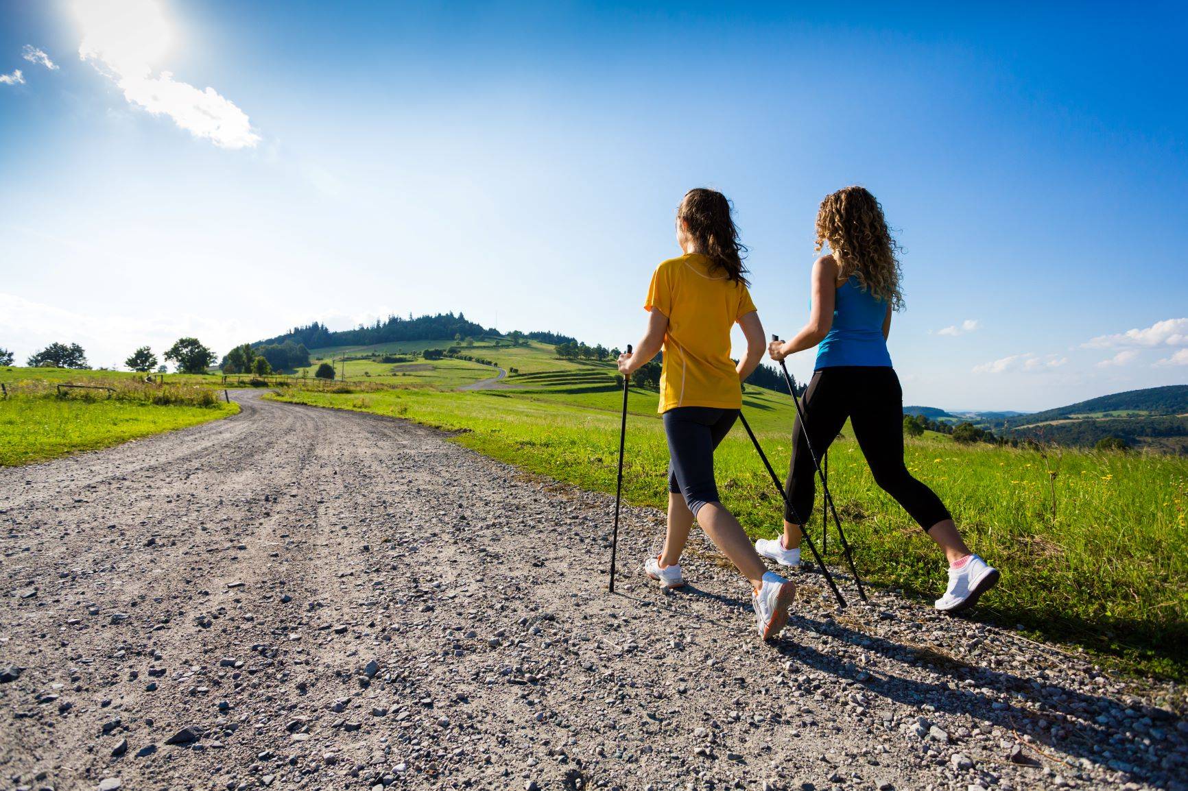 Czy strzykające stawy powinny martwić? Dwie kobiety w trakcie nordic walkingu latem na wsi.