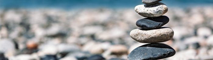 Duchowy aspekt człowieka w medycynie chińskiej - jakie emocje oddziałują na jakie narządy i dlaczego mogą wywołać chorobę? Koncept zen - kamienie ustawione na sobie w równowadze na kamienistej plaży nad oceanem.