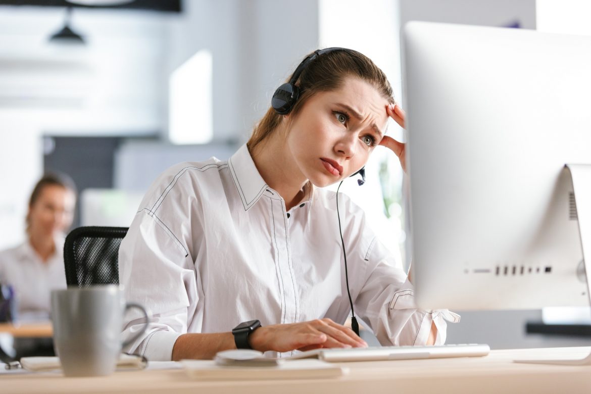 Przyczyny chronicznego zmęczenia. Młoda zmęczona kobieta siedzi przed komputerem ze słuchawkami na uszach.