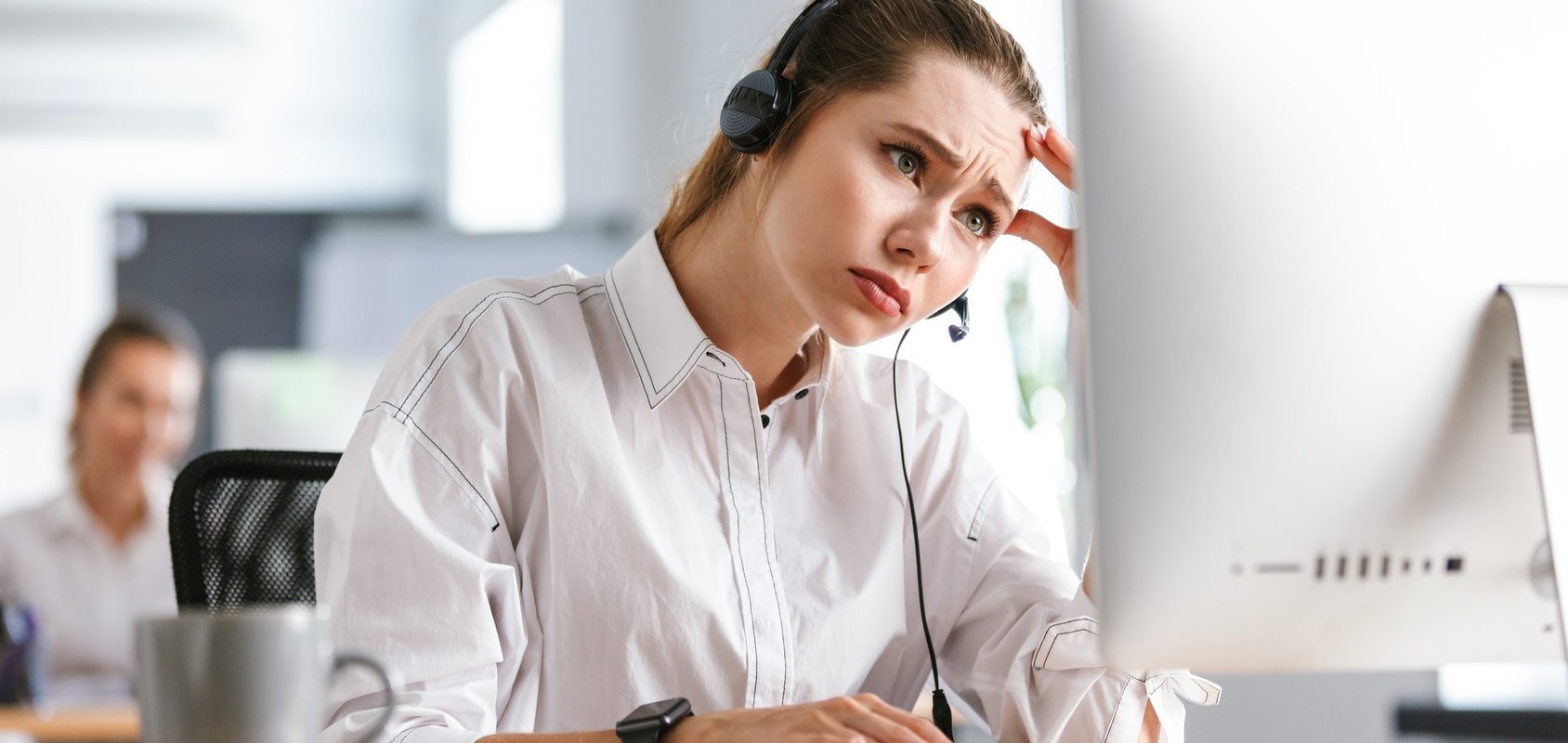 Przyczyny chronicznego zmęczenia. Młoda zmęczona kobieta siedzi przed komputerem ze słuchawkami na uszach.
