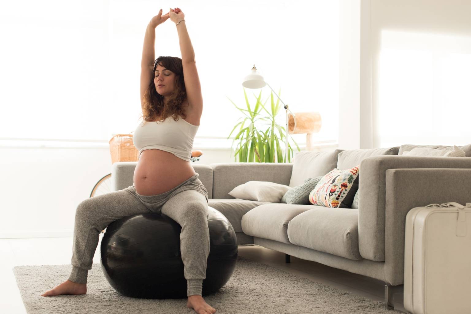 Kobieta w ciąży wykonuje ćwiczenia oddechowe na piłce w domu.